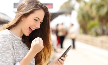 young woman outside with phone in hand happily making a fist and smiling at phone