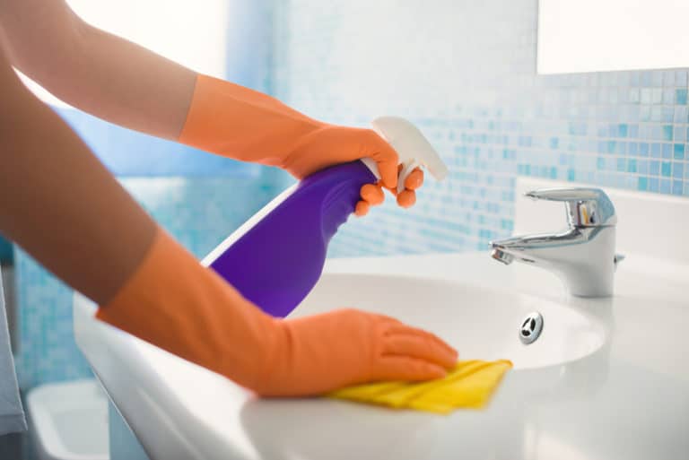 woman cleaning bathroom at home, cleaning sink and faucet with spray detergent.