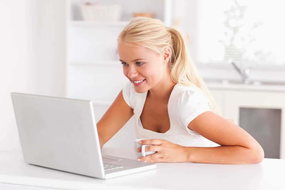 Tripwire Marketing: How to Make an Extra $250 Per Month 1 Cute woman having a cup of tea while using her notebook in her kitchen