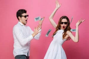 Portrait of a happy smartly dressed couple celebrating while standing under money shower isolated over pink background