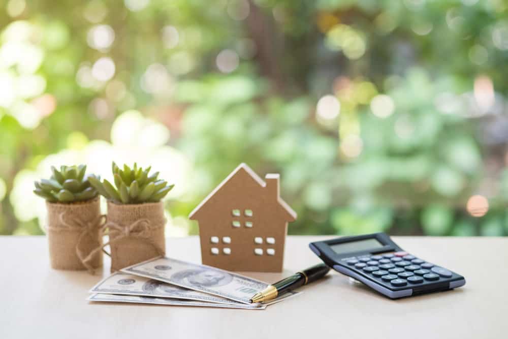 Should I Refinance My Debt? An Inside Look into an Important Decision 1 Home Loan, mortgage and real estate concept, House model with pile of dollar bills, calculator, pen and plant pots on table with garden background for business, finance, banking, and saving money.