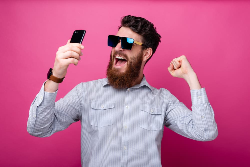 10 Best Cheap Cell Phone Plans (How to Save the Most) 1 Portrait of amazed bearded man in casual holding smartphone and celebrating victory