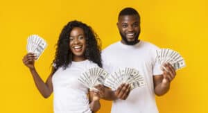 Cheerful Black Couple Holding Money, yellow studio background, panorama