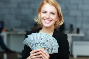 businesses to start with $10K Happy smiling businesswoman holding bills of dollars in office