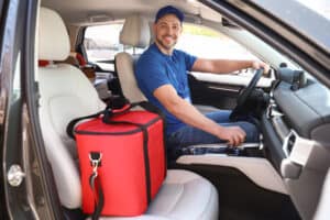 doordash vs. grubhub Male courier with thermo bag in car. Food delivery service