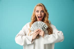 how much is 5 figures Portrait of a delighted young blonde woman in sweater showing money banknotes isolated over blue background