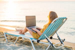 Get Paid To Travel, Fit young woman sitting on deck chair at sea view beach using laptop