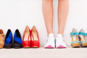 sell shoes online I made my choice! Cropped image of woman in sports shoes standing against the wall while high hilled shoes laying in a row near her