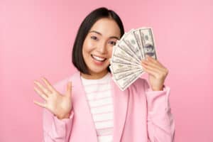 Free Money Hacks Microcredit, investment and business people concept. Young asian businesswoman, corporate lady showing money, cash dollars, waving hand, pink background.
