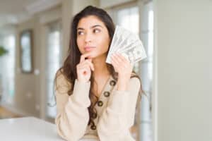 How To Make 20 Dollars Fast Young woman holding 20 dollars bank notes serious face thinking about question, very confused idea