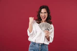 How To Make $5000 A Month Picture of positive smiling young woman isolated over red wall background holding money make winner gesture.