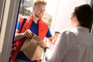 How To Make $500 A Week With DoorDash, Courier giving order to young woman at open door.